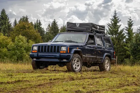 Jeep off-roading in Asiago, Italy, surrounded by lush trees and cloudy skies.