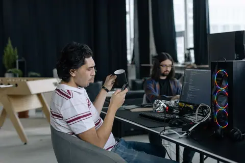Two programmers at work in a modern office, focused on coding and enjoying a coffee break.