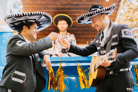 Mexican musicians wearing sombreros toast with tequila, celebrating in traditional attire.