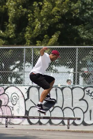 Skateboarder performing a trick on a rail at a graffiti-adorned skate park.