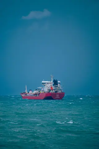 A solitary red cargo ship sails on the turquoise sea under a clear blue sky.