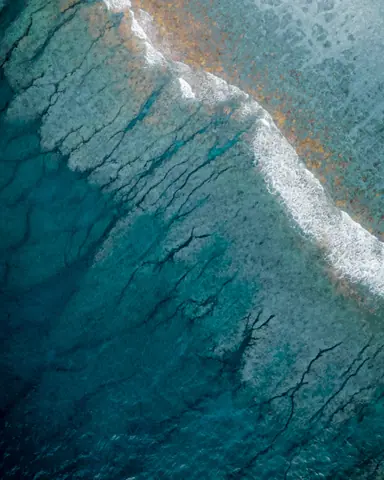 Aerial view of ultramarine sea waves with narrow stripe of white foam washing coastline