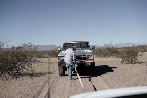 Man assisting stranded pickup truck in arid desert setting.