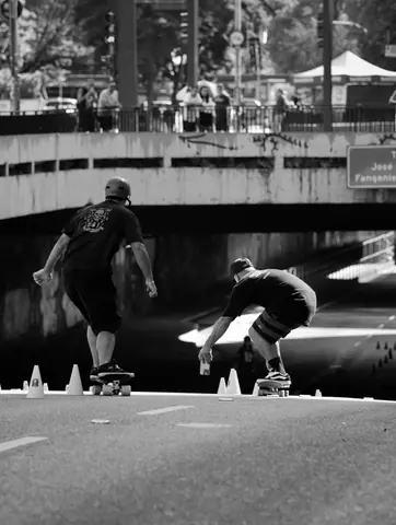 Two skateboarders navigate urban cones in a dynamic, black and white street scene.