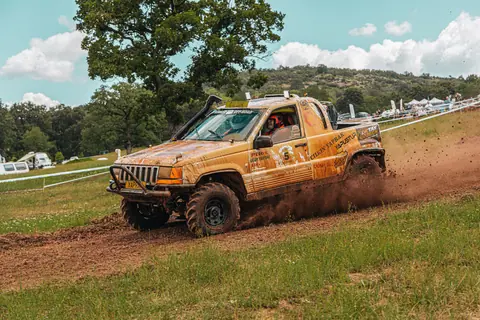 Thrilling offroad vehicle race on a muddy track amidst a lush countryside landscape under a bright sky.