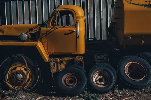 An aged yellow truck surrounded by old tires in an industrial setting, exuding vintage charm.