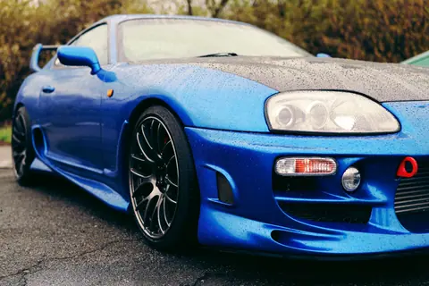 Dynamic low-angle shot of a blue sports car covered in raindrops, emphasizing its sleek design.