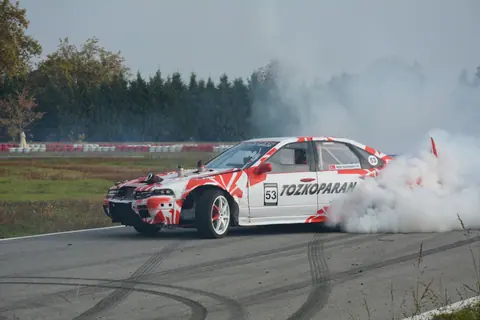 A race car performing an impressive drift on a track, surrounded by smoke.