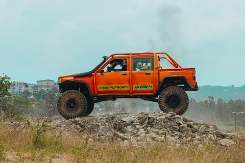 An orange off-road truck conquers rugged terrain in an exciting outdoor race, showcasing power and adventure.