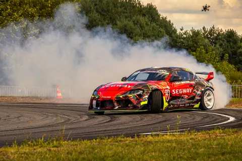 A dynamic car drifts with smoke on a race track surrounded by nature, capturing speed and power.
