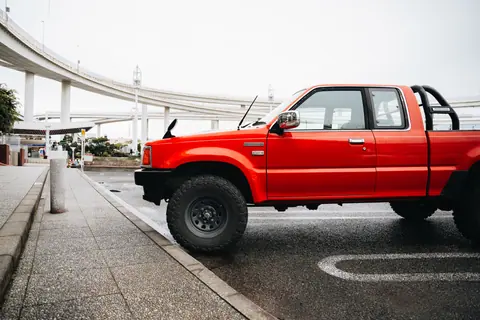 A vibrant red classic truck parked on a city street with elevated roads in the background.