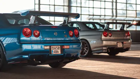 Two Nissan Skyline GTRs parked indoors in Roskilde, Denmark with sunlight filtering through windows.