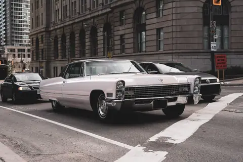 Old timer car driving on asphalt roadway near stone building facade in town