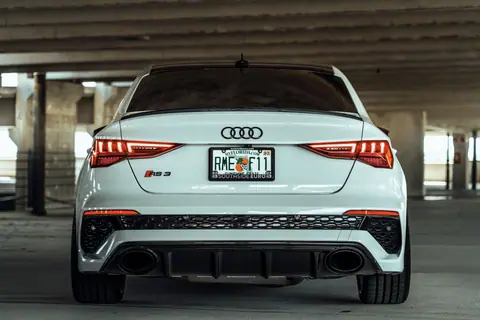 A sleek white Audi RS3 with Florida license plate parked in an urban parking garage.