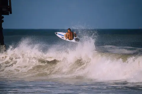A surfer skillfully rides a wave, displaying agility and balance against a vibrant ocean backdrop.