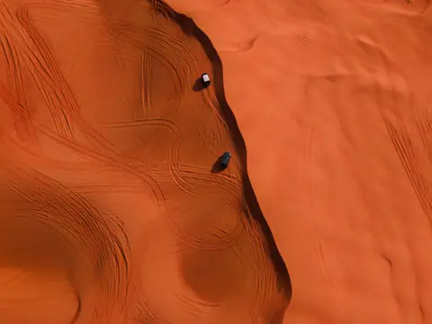 Stunning aerial shot of two cars making tracks on vibrant red sand dunes in a desert landscape.