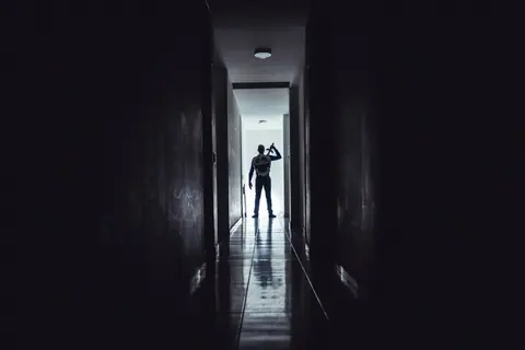 Dark, dramatic silhouette of a man holding a sword in a narrow hallway, creating an intense atmosphere.