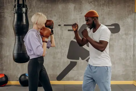 A boxing trainer coaches a female athlete during a training session indoors.