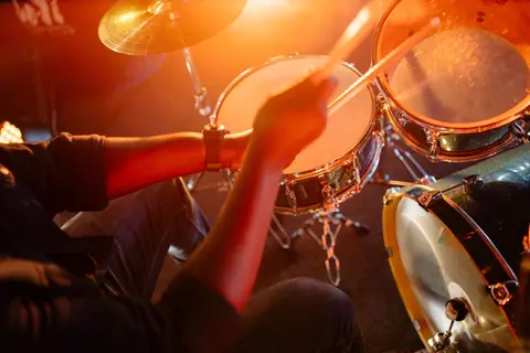Dynamic shot of a drummer playing under warm stage lighting, showcasing energy and rhythm.