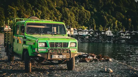 A vibrant green truck parked by a river in Arhavi, Türkiye, with a forest backdrop.
