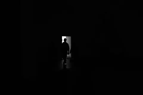 A shadowy figure stands silhouetted in a doorway, outlined by bright light.
