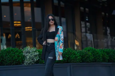 Chic fashion portrait of a woman in sunglasses and a colorful jacket in the city.