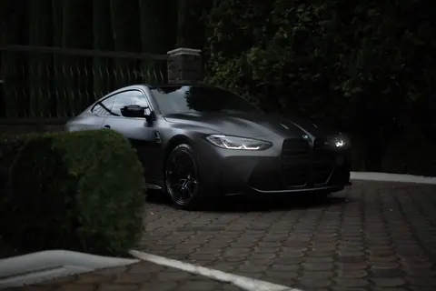Black sports car parked outdoors on a paved surface with greenery around.