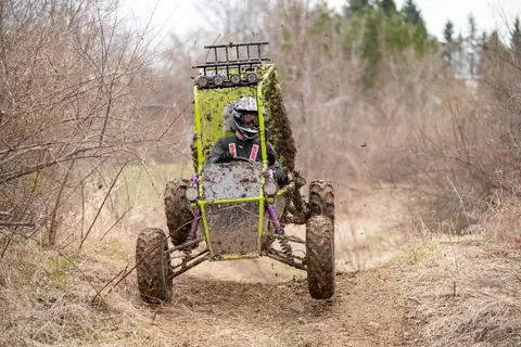 Dynamic off-road racing in a rugged, muddy terrain with a dirt-splattered buggy and driver.