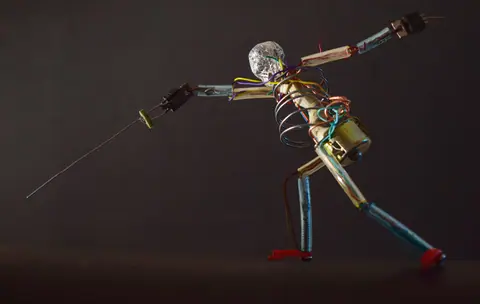 Metallic robot sculpture in a dynamic fencing pose with wires and parts, shot in São Paulo.