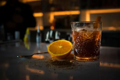 A stylish cocktail with a sliced orange, ice, and bar ambiance creates a sophisticated vibe.