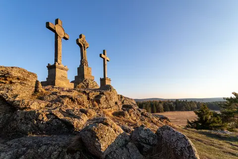 Three stone crosses on rocky hill in Prameny, rural Czech Republic landscape, against clear sky.