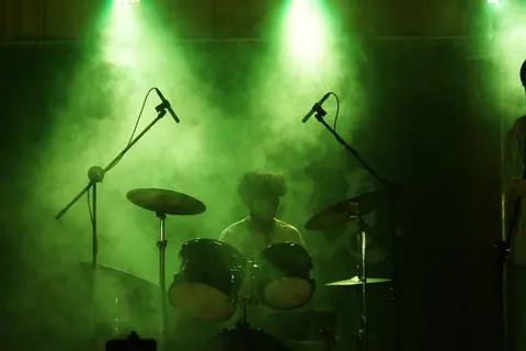 A drummer performs on stage amid smoke and green lights, creating a vibrant concert atmosphere.