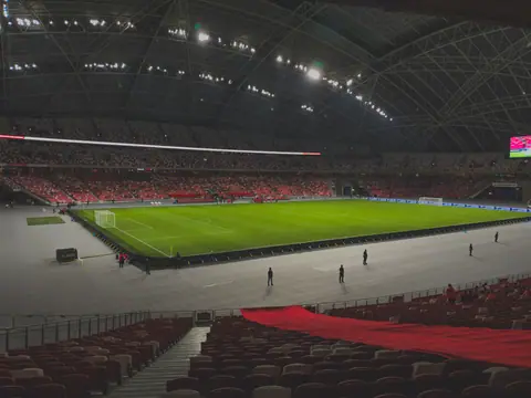 Spacious indoor soccer stadium filled with spectators. Bright lighting enhances the green field.