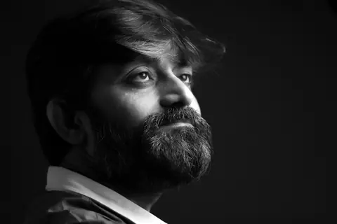 A striking black and white portrait of a contemplative bearded man on a dark background.