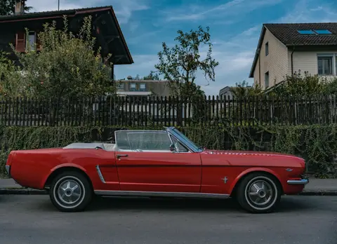 A vintage red Ford Mustang convertible parked on a quiet city street, capturing a classic urban vibe.