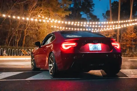 A red sports car under string lights on a festive night road scene.
