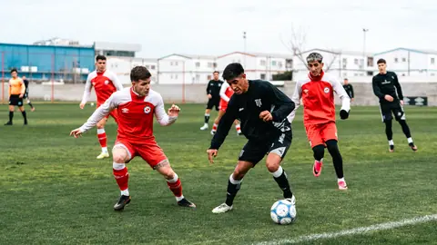 Players in red and black uniforms compete vigorously in a soccer match outdoors.