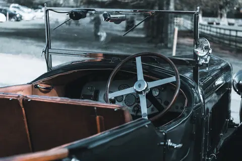 Interior view of a classic vintage convertible car featuring a wooden steering wheel and soft leather seating.