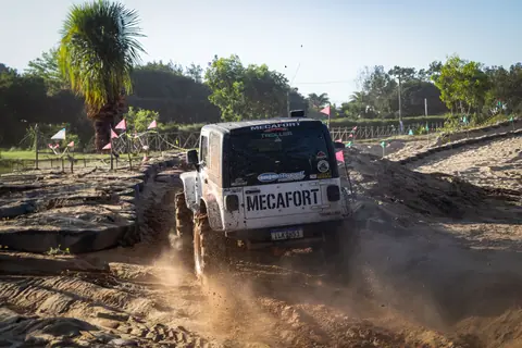 4x4 vehicle driving on a sandy off-road track, creating a dust trail in a sunny, green environment.