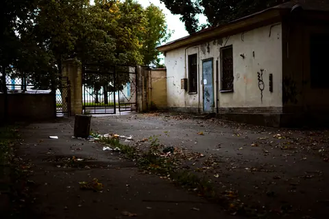 Moody scene of an abandoned, weathered house in an urban backyard amidst fallen leaves.