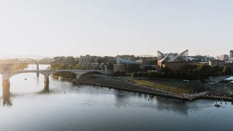 Scenic aerial view of Chattanooga's riverfront and bridges at sunset, showcasing city landmarks and waterfront activities.