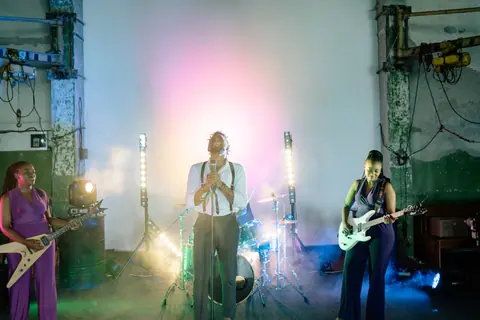 Dynamic indoor band performance with singers and guitarists under vibrant lighting and smoke effects.