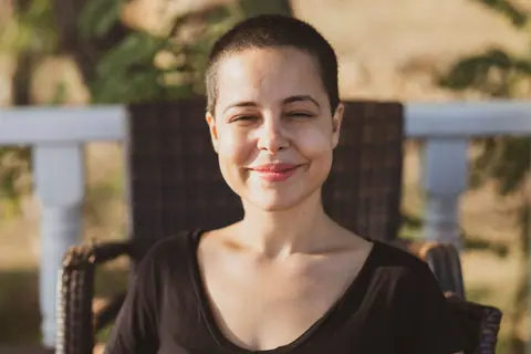 A young woman with a buzz cut enjoys the summer sun, her smile radiating happiness and relaxation.