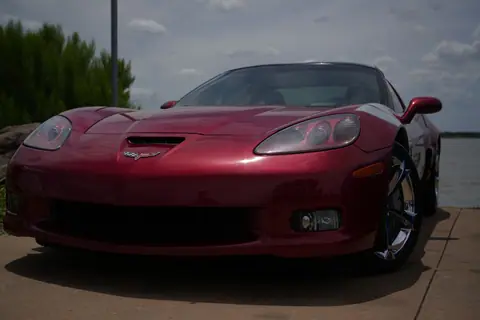 Front view of a shiny red sports car by the river under a cloudy sky. Perfect for car enthusiasts.