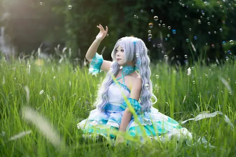 A cosplayer in a mystical costume sits in a meadow surrounded by glowing bubbles and vibrant greenery.