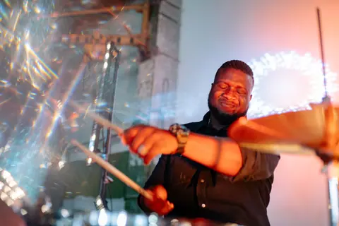 Drummer passionately playing during a lively music performance with vibrant lights.