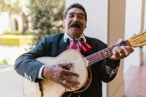 A cheerful Mexican musician in traditional attire playing a guitar outdoors.