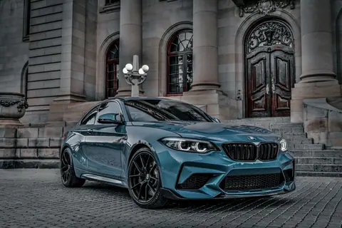 Stylish BMW M2 parked outside a classical building, displaying luxury and elegance.