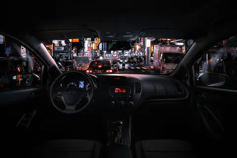 View from car interior at night in Tokyo, featuring bustling street traffic and illuminated cityscape.