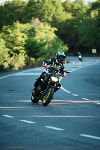 A motorcyclist in gear takes a turn on a scenic winding road, surrounded by lush greenery.